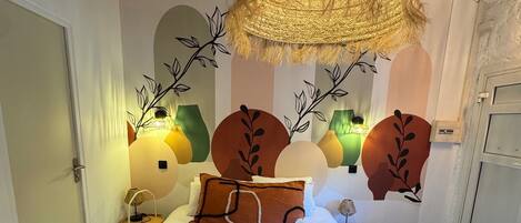 Una habitación de hotel con una cama grande, detalles decorativos en la pared y una lámpara de techo tejida y original.