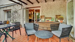 Une terrasse extérieure dotée d’un mur en pierre rustique, d’un plafond en bois et d’un espace détente avec deux chaises et une table.