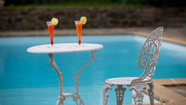 A poolside table with two drinks, a chair, and a decorative metal chair. - Hôtel Au Petit Breuil (La Courtine)