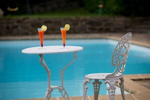 A poolside table with two drinks, a chair, and a decorative metal chair.