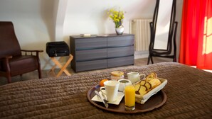 A neatly made bed with a tray of breakfast items including toast, a muffin, a cup of coffee, a glass of orange juice, and a small bowl of yogurt. - Hôtel Au Petit Breuil (La Courtine)