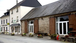 A stone building with wooden shutters, a sign for 'Le Petit Restaurant', and outdoor seating with potted plants. - Hôtel Au Petit Breuil (La Courtine)