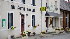 A building with a sign reading "Au Petit Breuil" and another sign for "Hotel Restaurant". There are flower pots on the sidewalk and a chair outside the building. - Hôtel Au Petit Breuil (La Courtine)