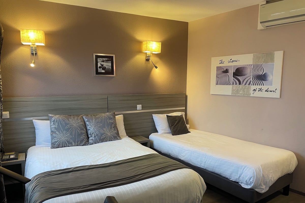 A hotel room with two beds, wall-mounted lamps, a framed picture, and a wall-mounted air conditioner.