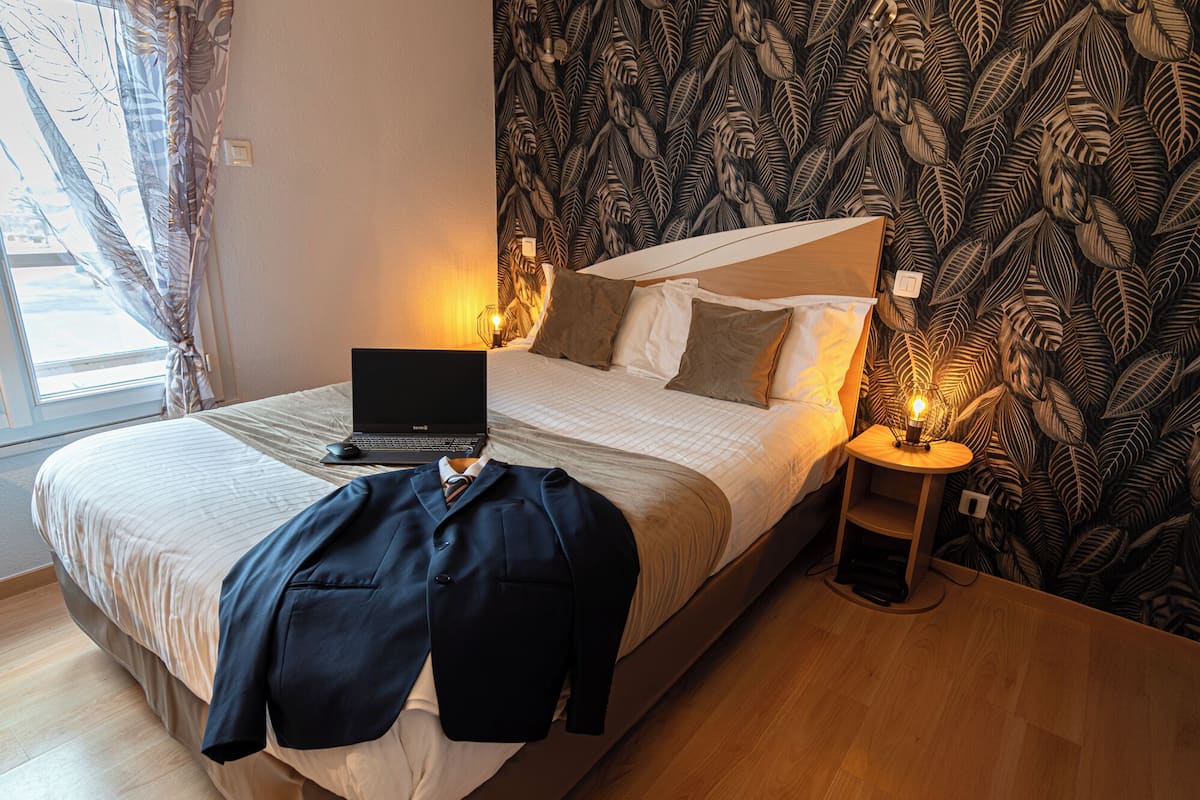 A neatly made bed with a laptop, a jacket, and a bedside lamp.