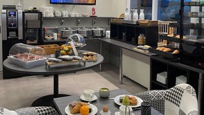 A modern breakfast area with a buffet, seating, and a TV displaying a cityscape. - Hostellerie du Centrotel et Spa (Montmarault)