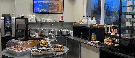 A modern breakfast area with a buffet, seating, and a TV displaying a cityscape.