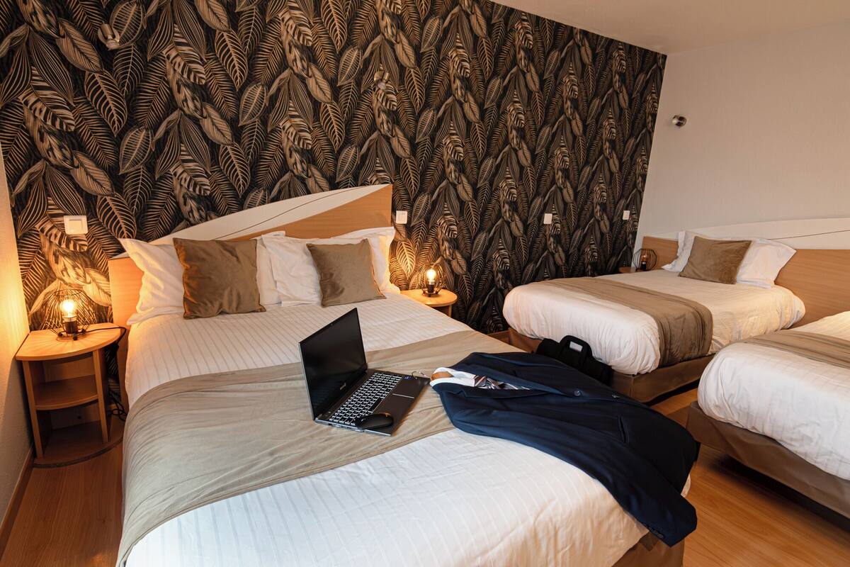 A hotel room with two beds, a laptop on the left bed, and a suitcase on the right bed.