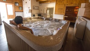 A hot tub with a person relaxing in it, wooden walls, and a tiled floor. - Hostellerie du Centrotel et Spa (Montmarault)