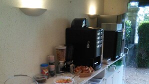 Un desayuno servido con una mesa cubierta por un mantel a cuadros, un frutero, una cafetera y diferentes condimentos.
