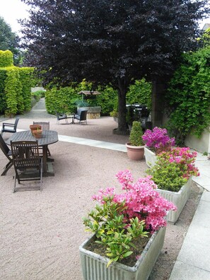 A patio area with a round table and chairs, surrounded by potted plants and a pergola. - Hôtel du Commerce (Tronget)
