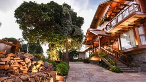 Un edificio de madera con un balcón, escalones de piedra y un gran árbol al fondo.