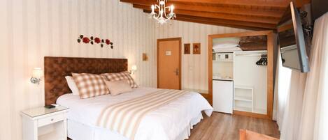 Ein Schlafzimmer mit Holzboden, einem Bett mit weißer Bettwäsche, einem Nachttisch, einer Kommode und einem Spiegel.