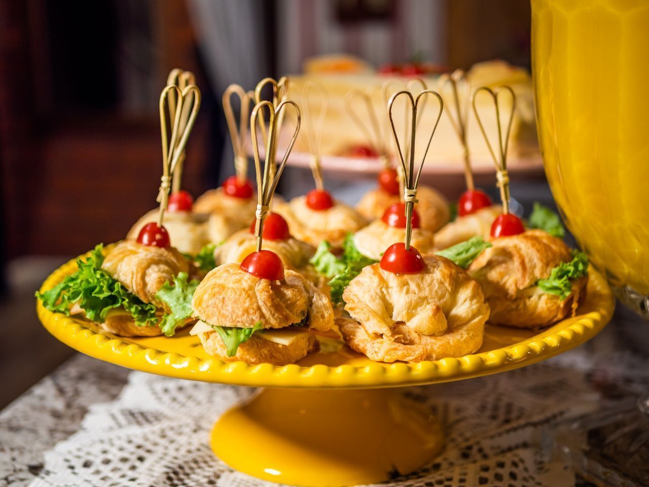 A yellow cake stand with mini sandwiches and cherries.