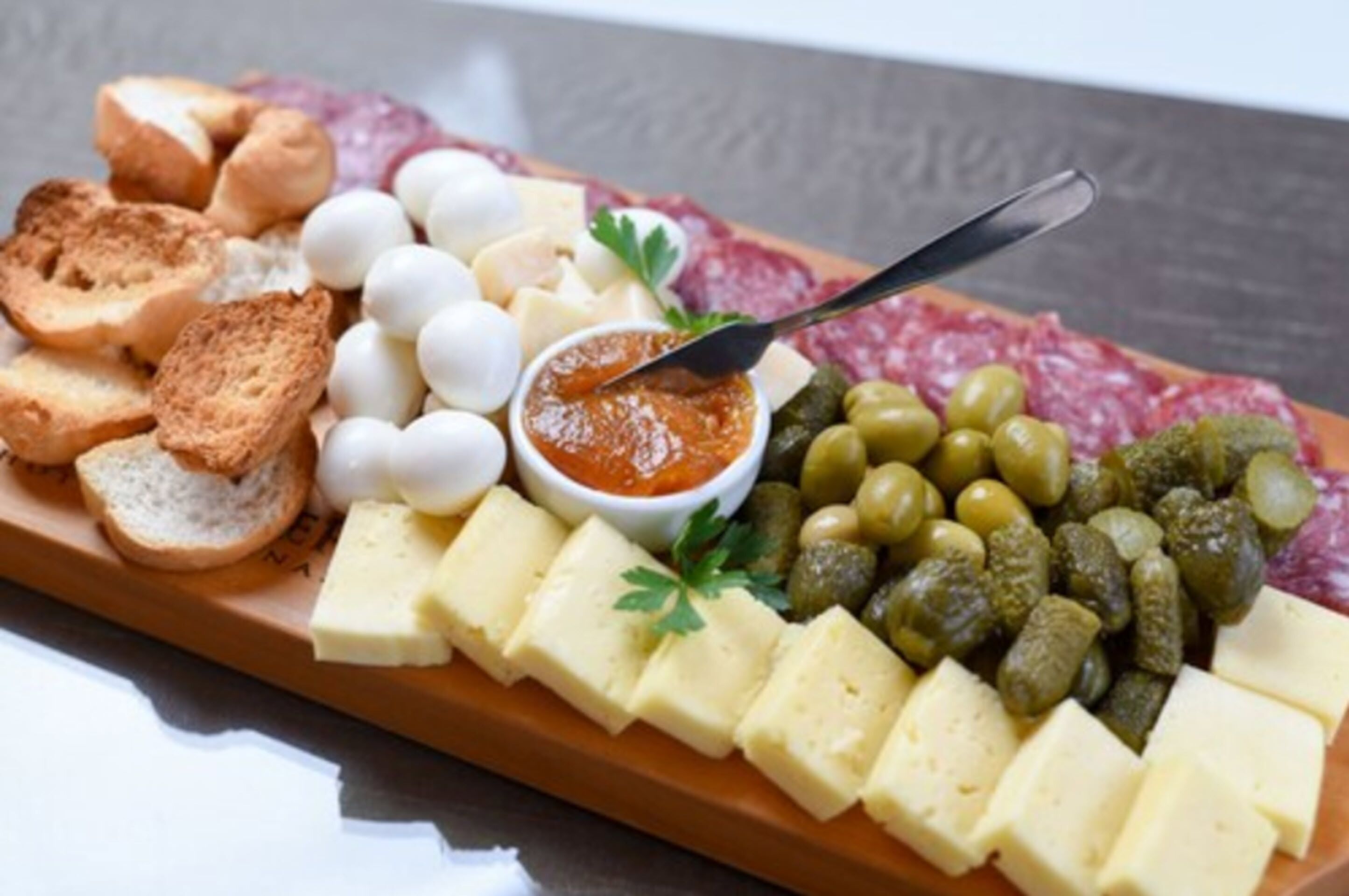 A charcuterie board with various cheeses, meats, olives, and bread.