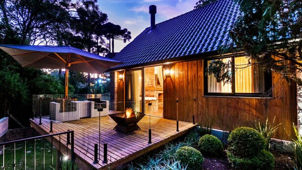 Una casa moderna con terraza de madera, una fogata y un área de estar al aire libre techada.