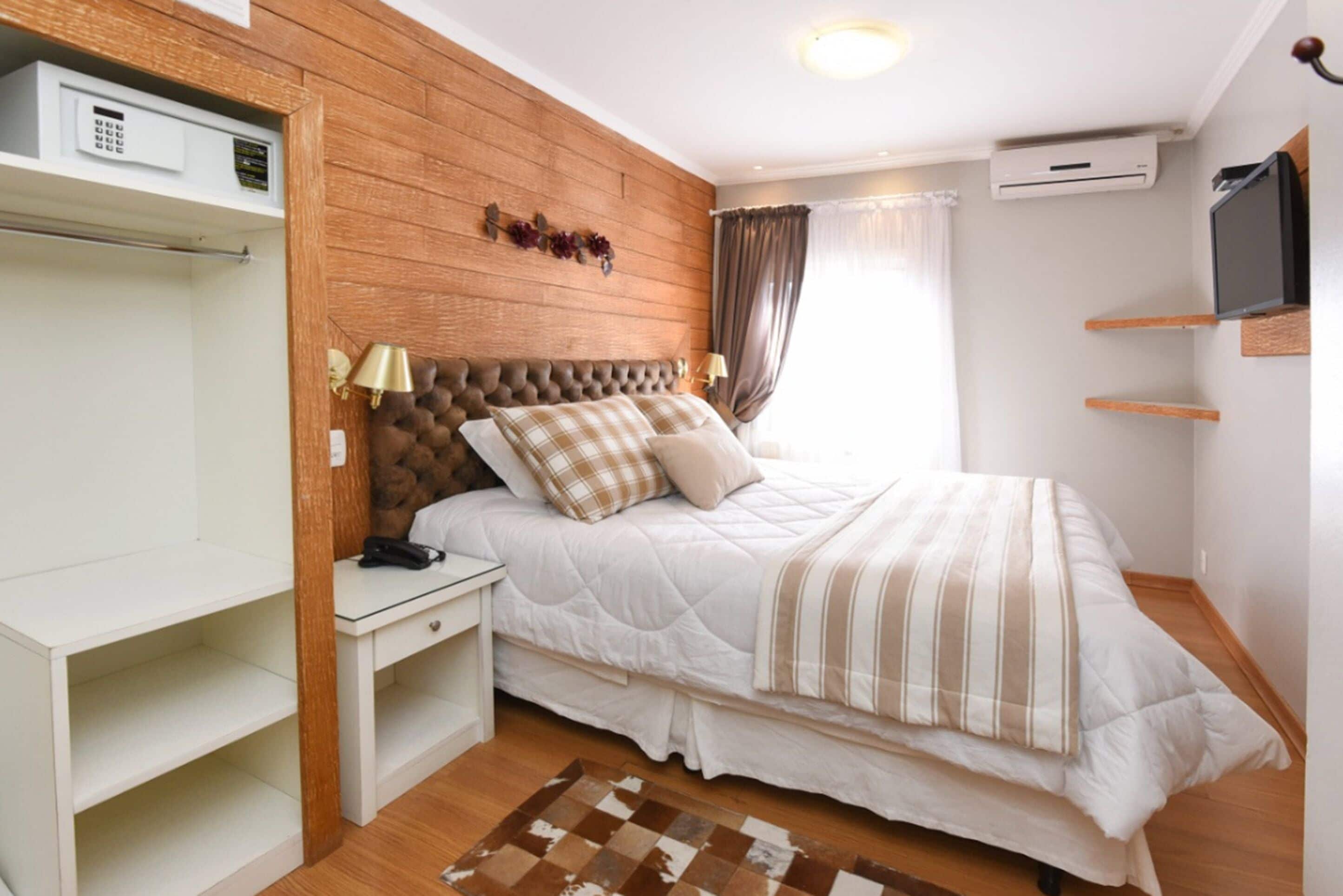 Un dormitorio con cabecera de madera, cama con ropa de cama a rayas, mesita de noche con lámpara y televisor montado en la pared.