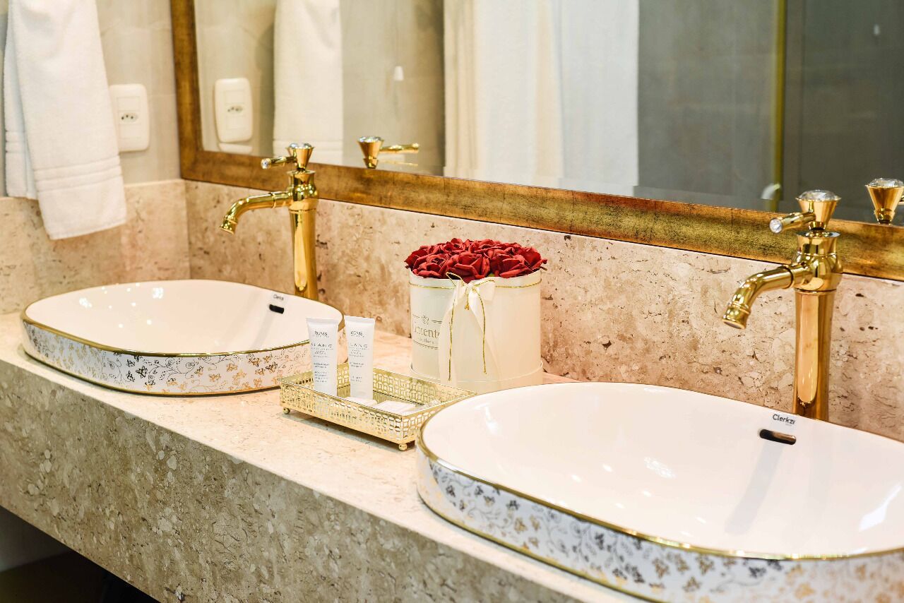 A bathroom with two sinks, a large mirror, and a vase of red roses.