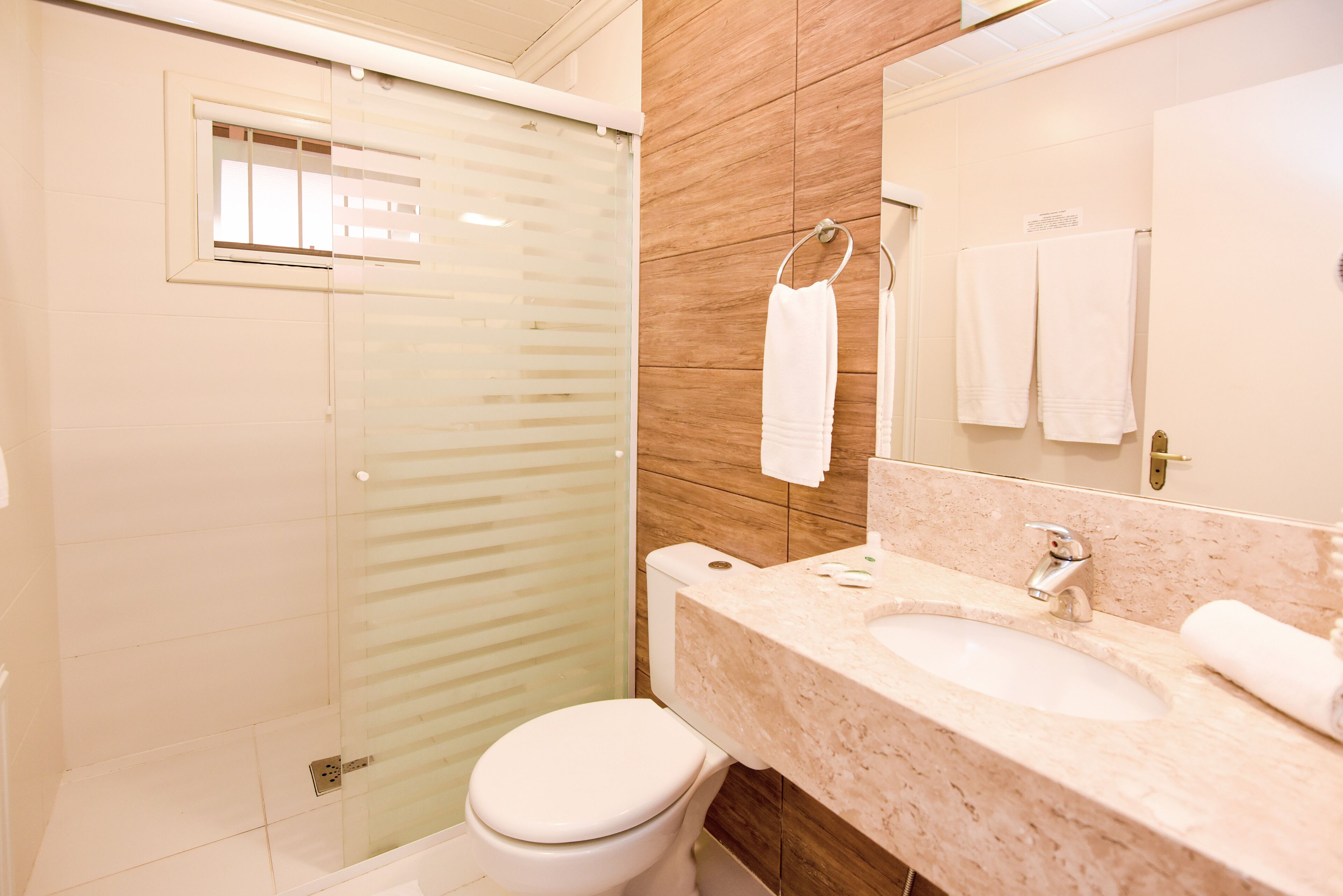 Un baño moderno con cabina de ducha de vidrio, inodoro blanco, lavamanos de mármol y un espejo grande.