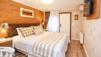 Une chambre à coucher avec une tête de lit en bois, un lit avec une literie à rayures, une table de chevet avec une lampe et un téléviseur fixé au mur.