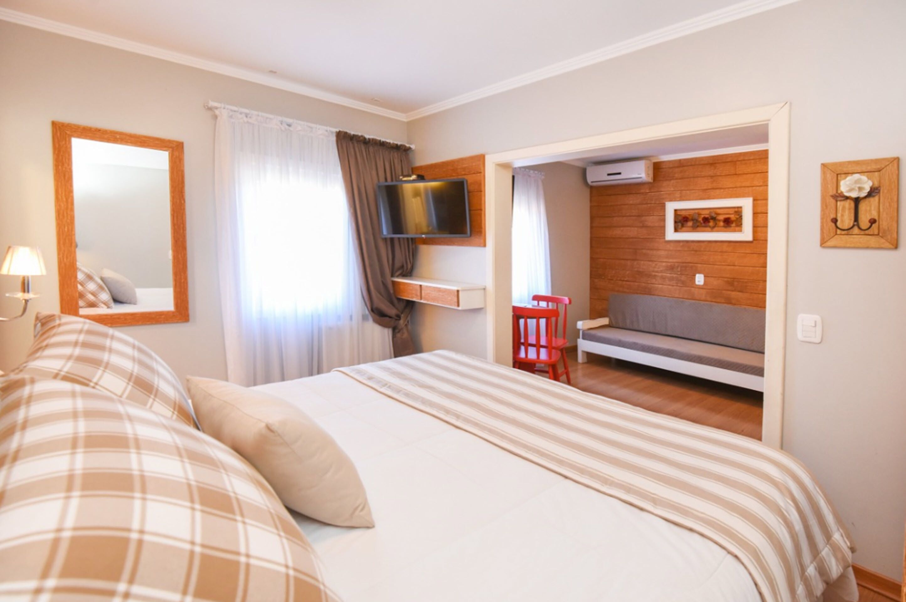 A bedroom with a bed, a TV mounted on the wall, a red chair, and a wooden panel wall.