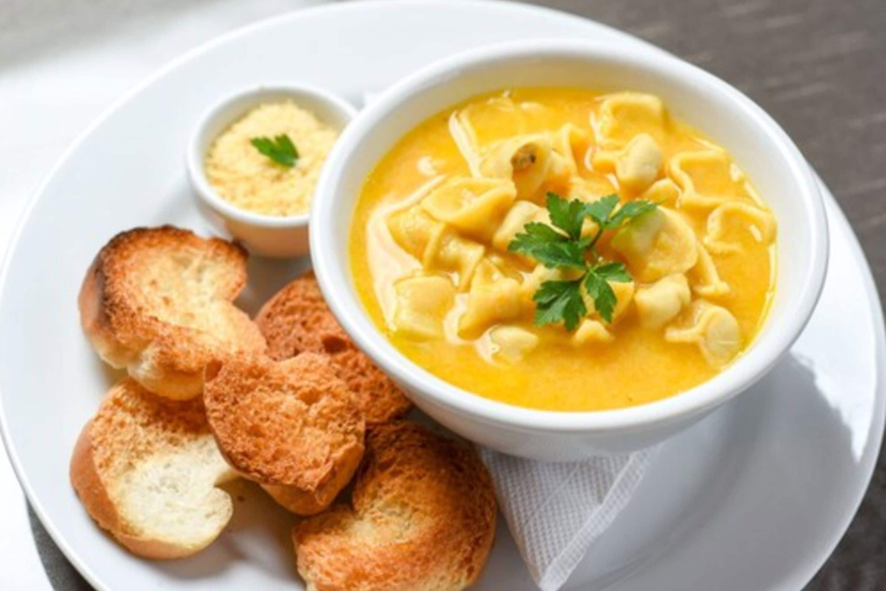 A bowl of soup with croutons and a garnish, accompanied by a small bowl of sauce and several croutons on a white plate.
