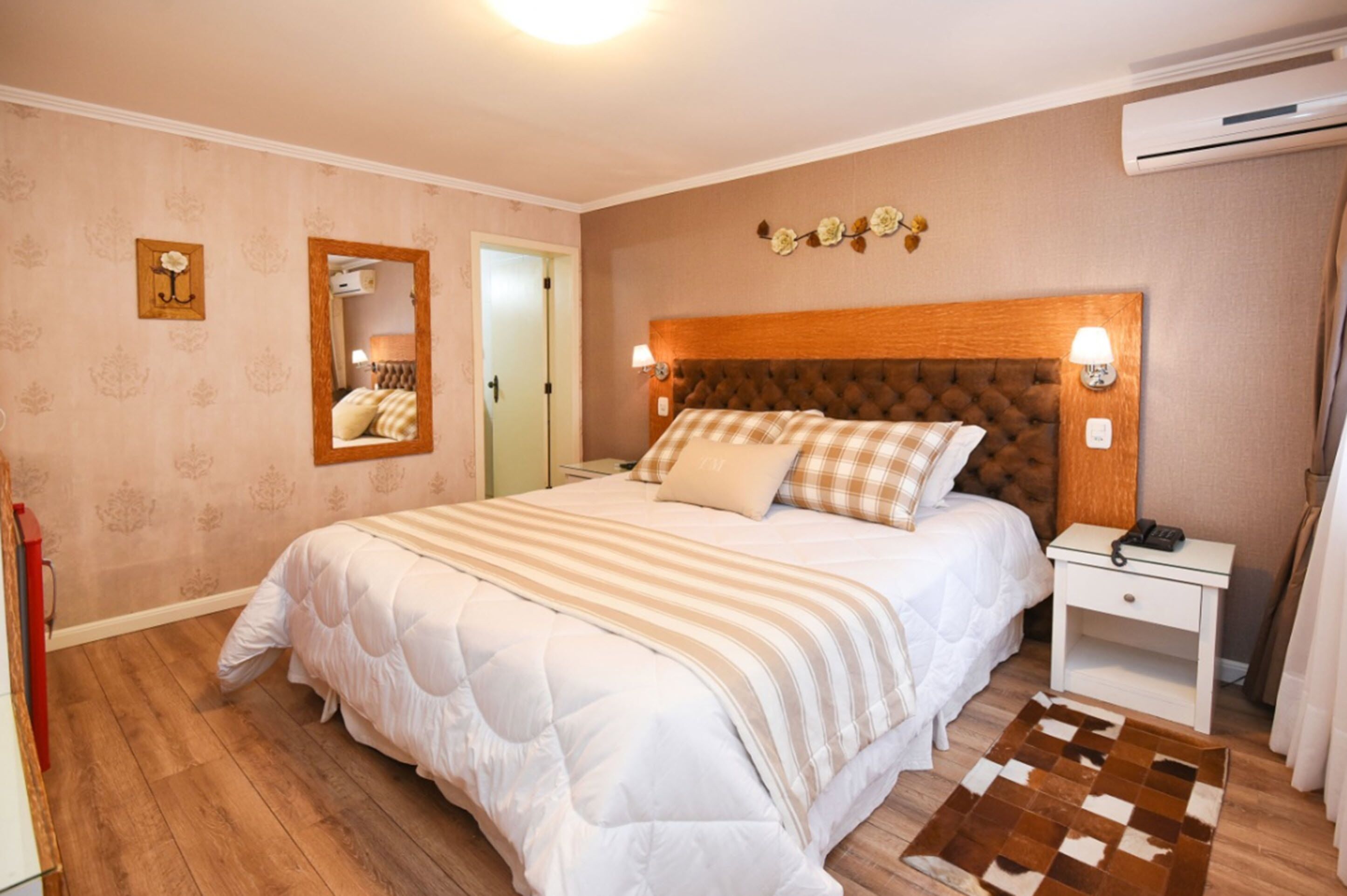 Un dormitorio con una cama grande, una mesita de noche, un espejo y un aire acondicionado instalado en la pared.