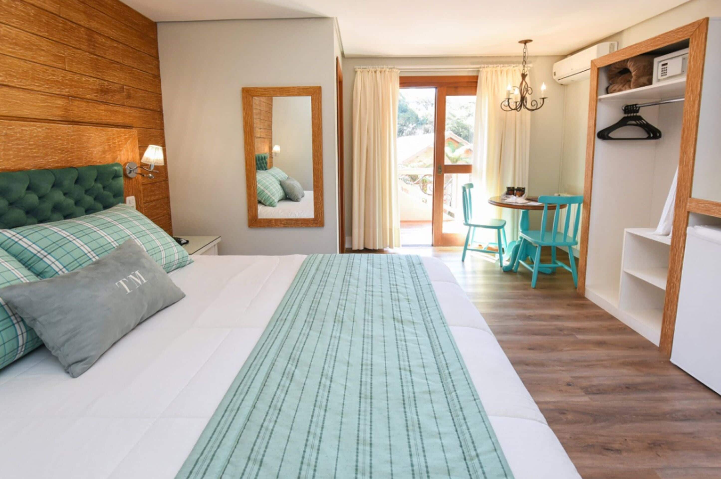 A bedroom with a large bed, a wooden headboard, a mirror, a desk with chairs, and a wardrobe.