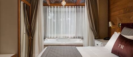 Habitación de hotel con una cama grande, cabecera de madera, mesita de noche con lámpara y vista a un área de spa.