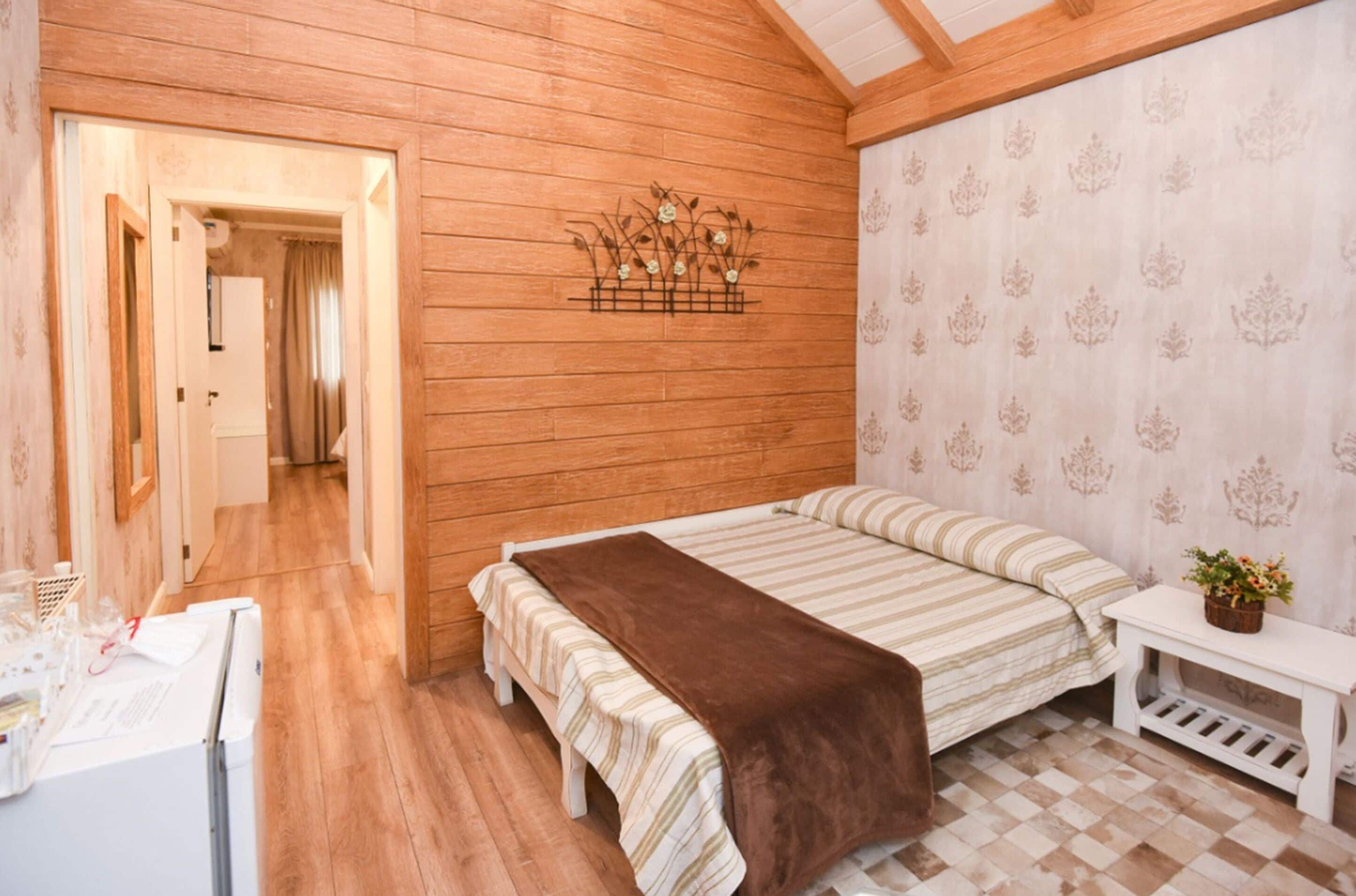 Ein gemütliches Zimmer mit Holzwänden, einem Bett mit gestreifter Bettwäsche, einem kleinen Nachttisch mit Pflanze und strukturierter Tapete.