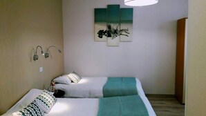 Une chambre avec deux lits, une lampe fixée au mur et un tableau.
