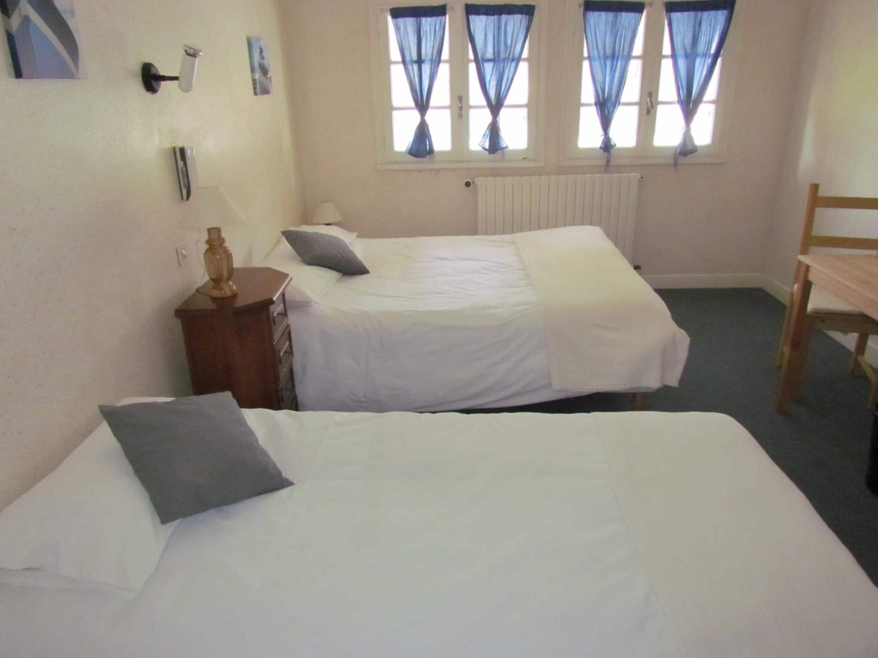 A room with two beds, a wooden chair, a dresser, and a window with curtains.