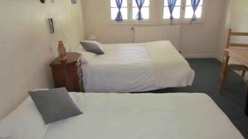 A room with two beds, a wooden chair, a dresser, and a window with curtains.