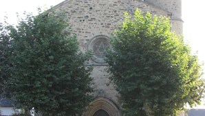 Une église en pierre dotée d’une entrée centrale en arc de cercle, d’un clocher et d’une grande fenêtre circulaire située au-dessus de la porte.
