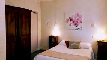 A bedroom with a large wooden wardrobe, a bed with white linens, a floral artwork on the wall, and bedside lamps.