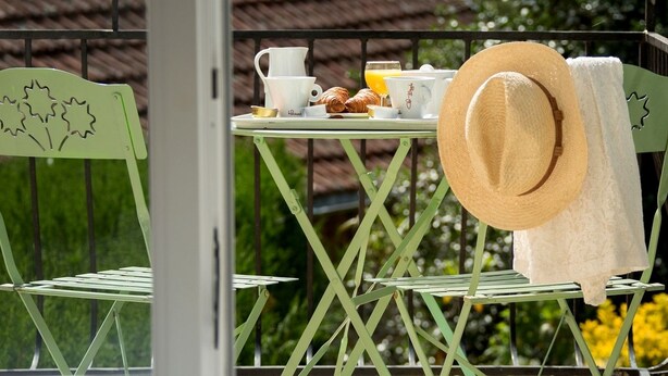 Un balcon avec une table préparée pour le petit-déjeuner, comprenant des croissants, des tasses à café et un verre de jus d’orange.