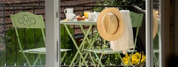 Uma varanda com mesa posta para o café da manhã, incluindo croissants, xícaras de café e um copo de suco de laranja.