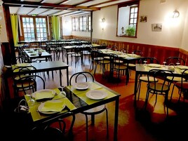 Uma área de refeições com várias mesas e cadeiras, disposta em um espaço amplo com grandes janelas que permitem a entrada de luz natural.
