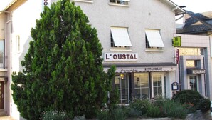 Un bâtiment portant une enseigne indiquant « L’OUSTAL » et « RESTAURANT », ce qui indique qu’il s’agit d’un établissement où l’on sert des repas.