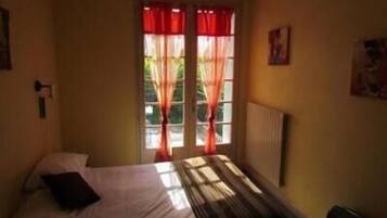 Une pièce avec un lit, un radiateur et une fenêtre ornée de rideaux rouges.