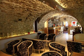 A cozy interior with stone walls, a bar area, and seating with floral upholstery. - Hôtel le Chêne Vert (Rocher)
