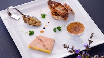 Un plato blanco con un trozo de salmón, un recipiente pequeño de salsa y una rebanada de pan sobre una superficie oscura.