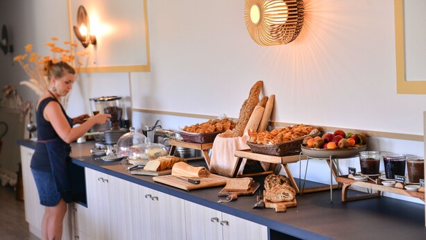 A buffet setup with various food items and a person preparing food. - Hôtel le Chêne Vert (Rocher)