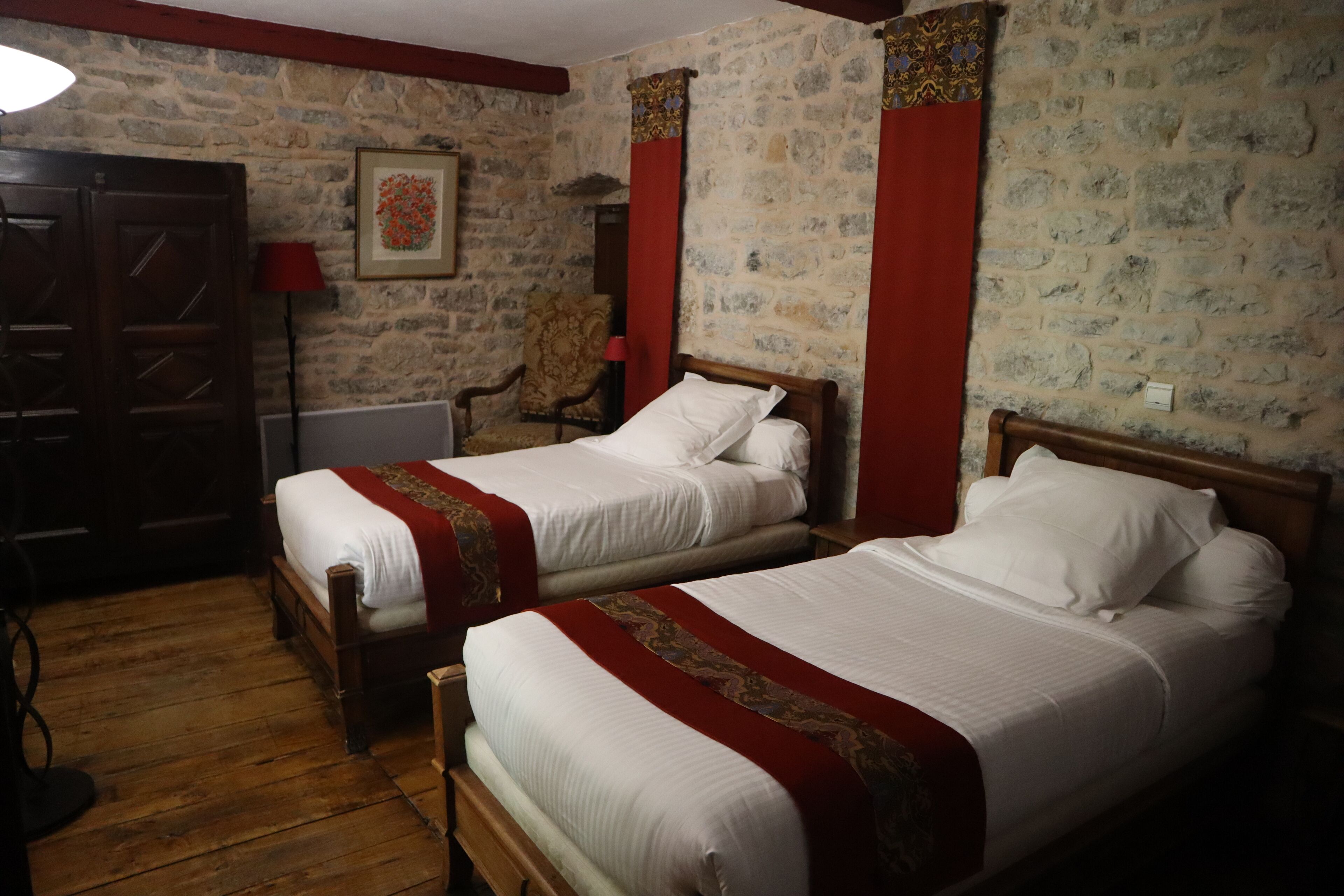 A room with two wooden beds, a stone wall, a red chair, and a wooden wardrobe.