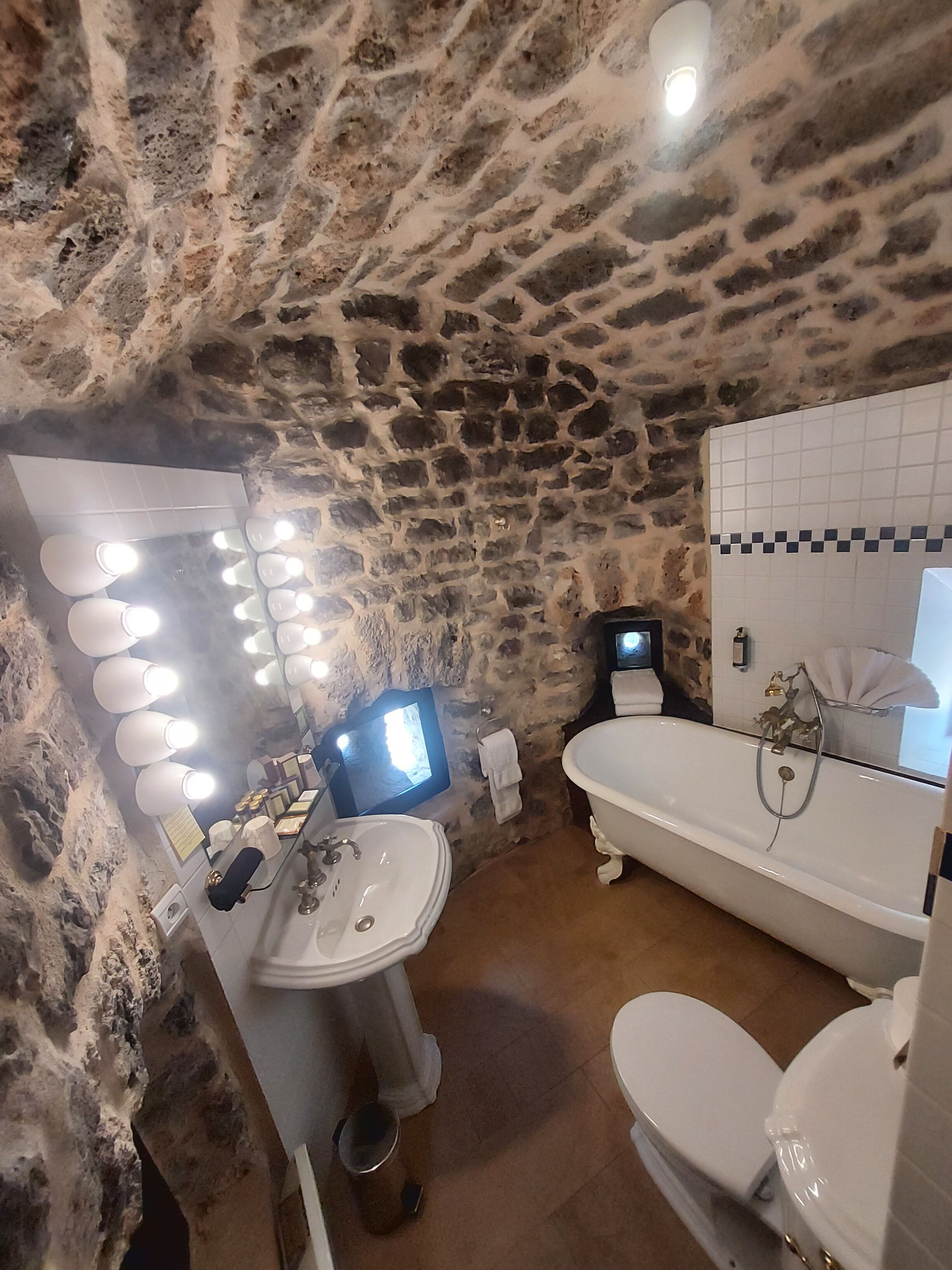 Une salle de bain avec un mur en pierre, un lavabo, une baignoire et des toilettes.