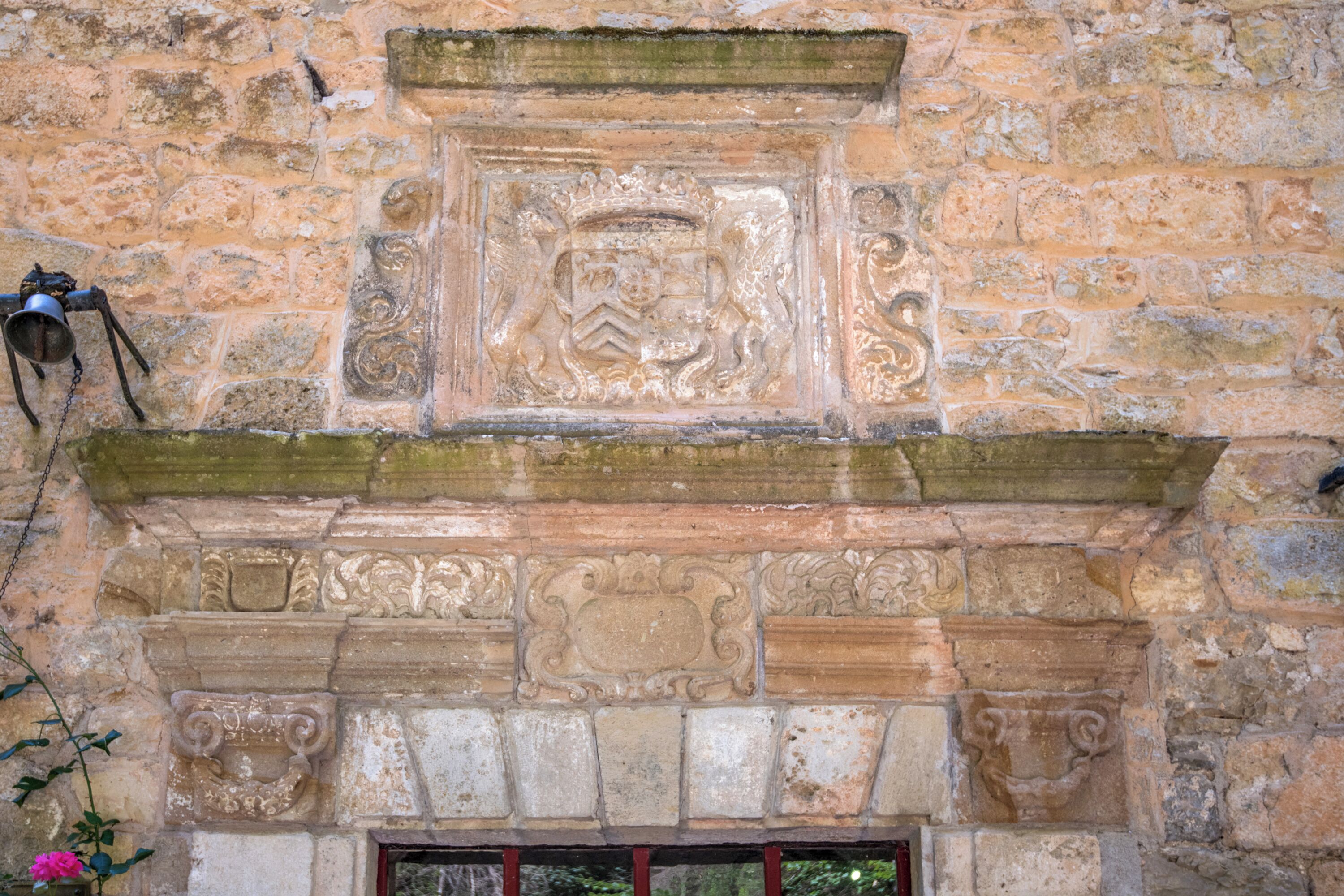 Un mur de pierre orné d’un blason sculpté et d’une cloche.
