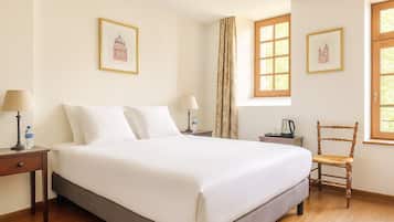 A hotel room with a large bed, two bedside tables with lamps, a wooden chair, and two windows with curtains.