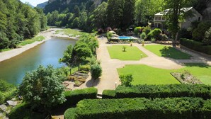 Un hotel junto al río con piscina, jardines cuidados y vistas al río y montañas circundantes.