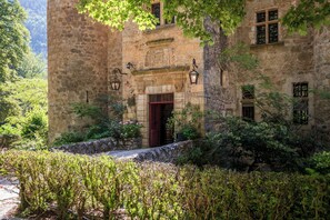 A stone building with a red door, surrounded by lush greenery and a stone wall. - Château de la Caze (Gorges du Tarn Causses)