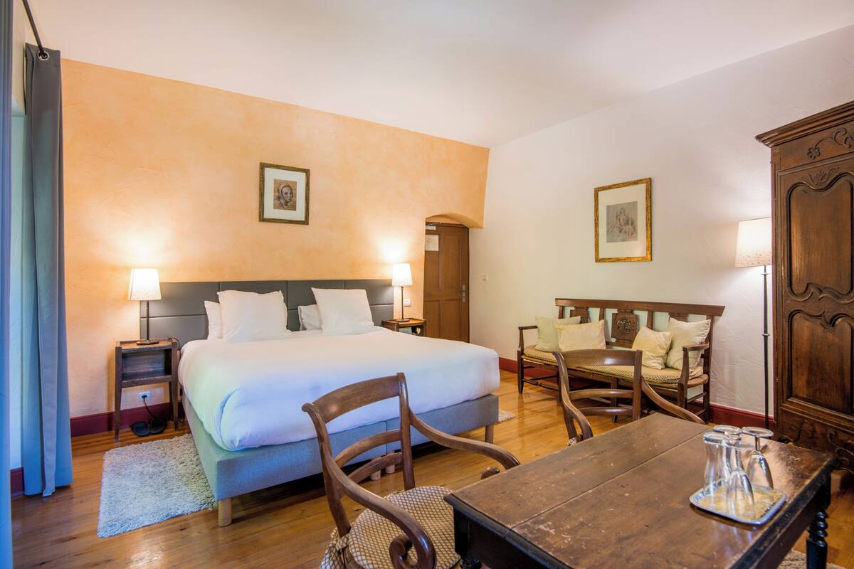 A hotel room with a bed, bedside tables, a wooden chair, a table with a pitcher, and a wardrobe.